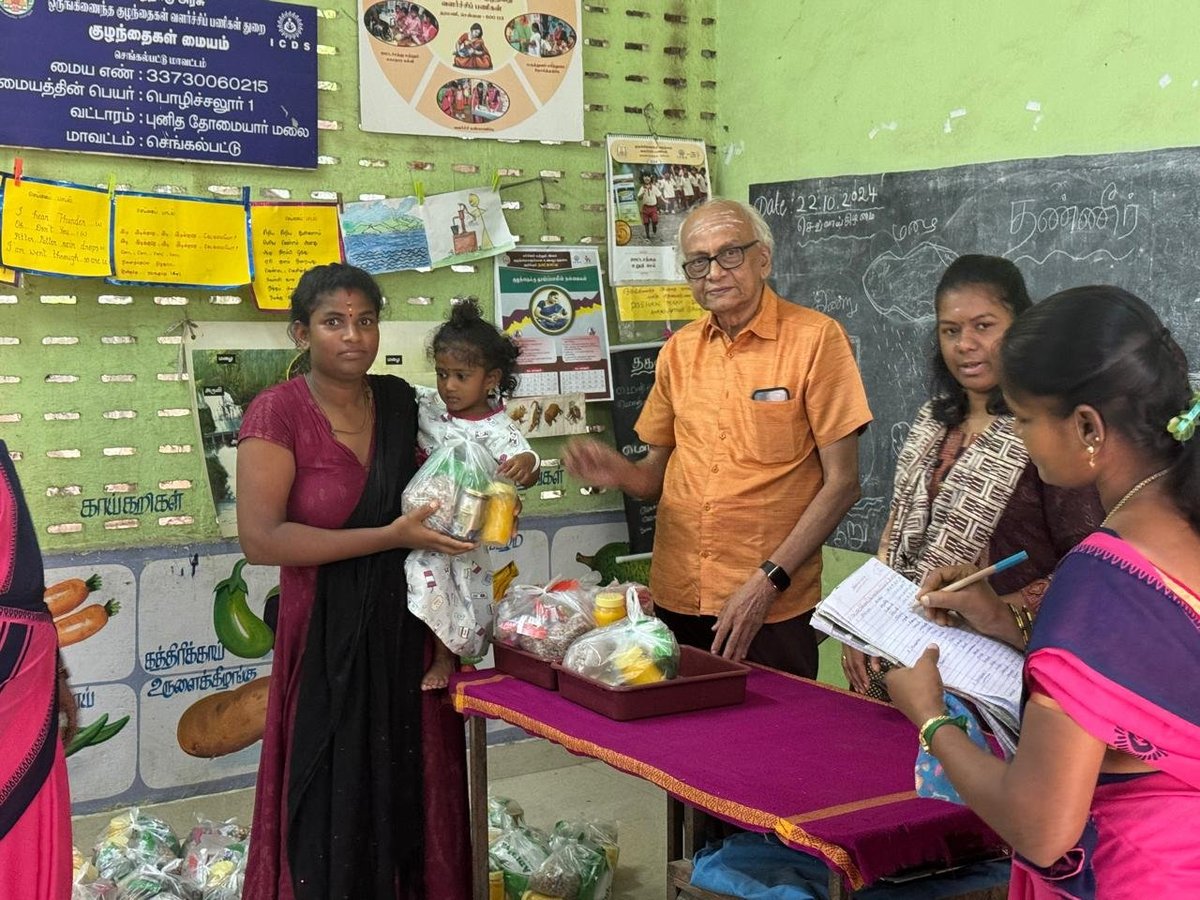 A group of people in a bright green classroom sharing and discussing food items around a table for what appears to be a community or educational event