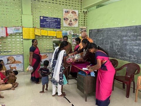 Teachers in bright pink saris help children in a classroom with lime green walls and educational materials displayed