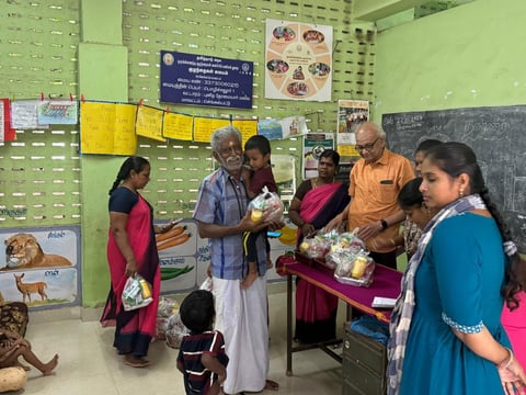 Community gathering in classroom with adults and children receiving items from volunteers in colorful clothing